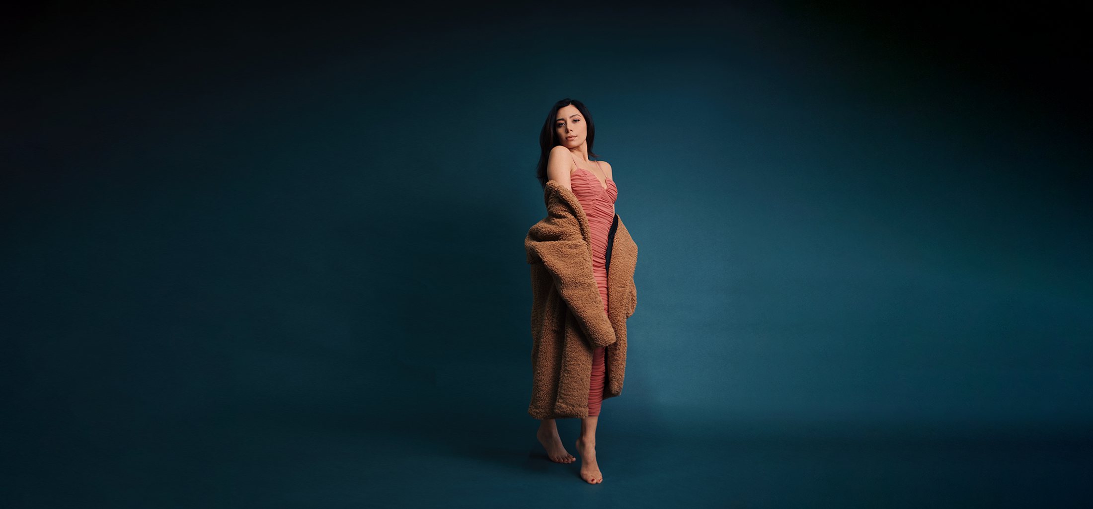 Full-length studio portrait against a deep teal backdrop.