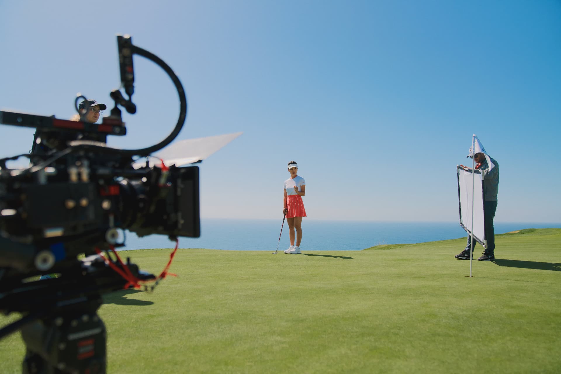 Talent on the ocean-side green with camera and flag in frame.