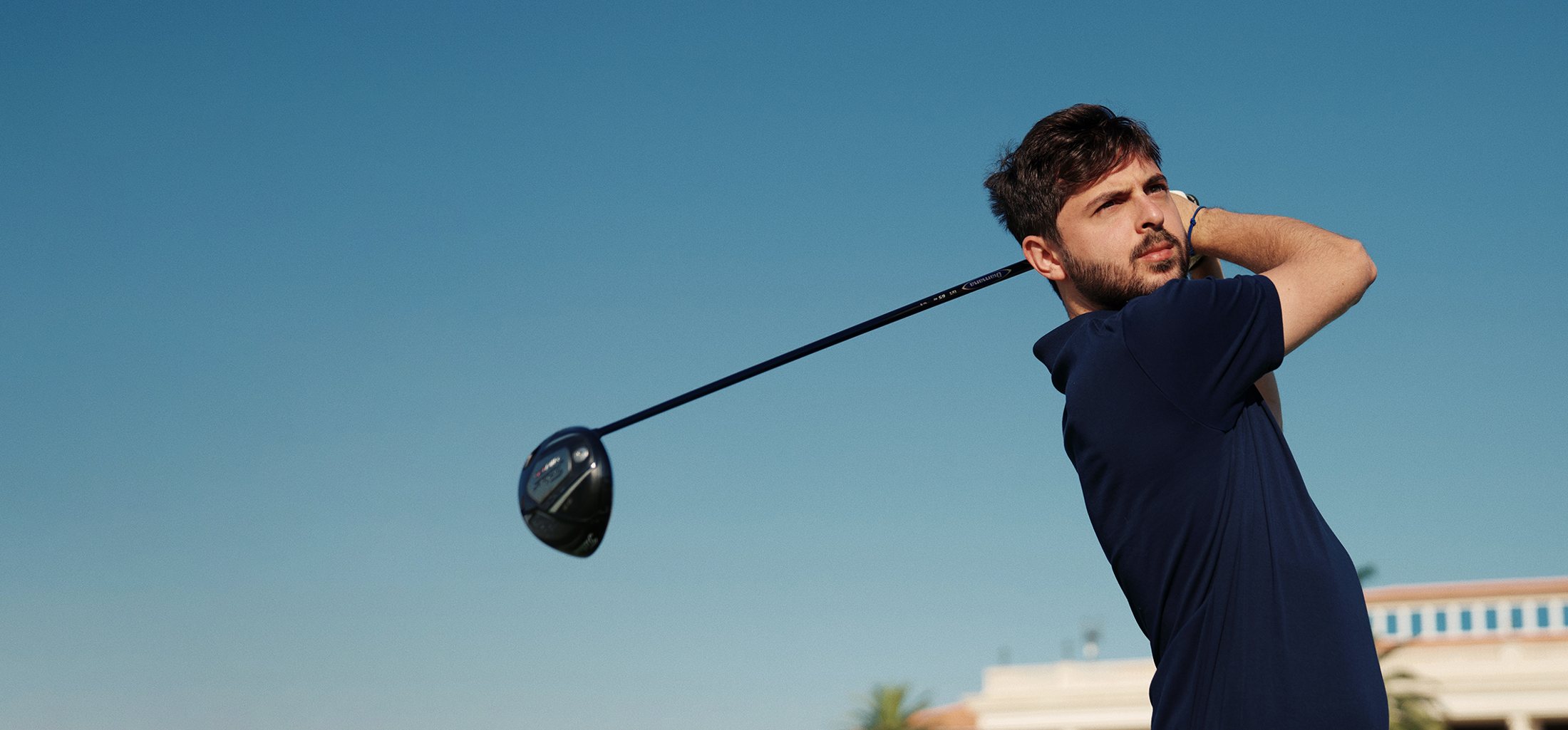 Golfer photographed mid follow-through against open sky.