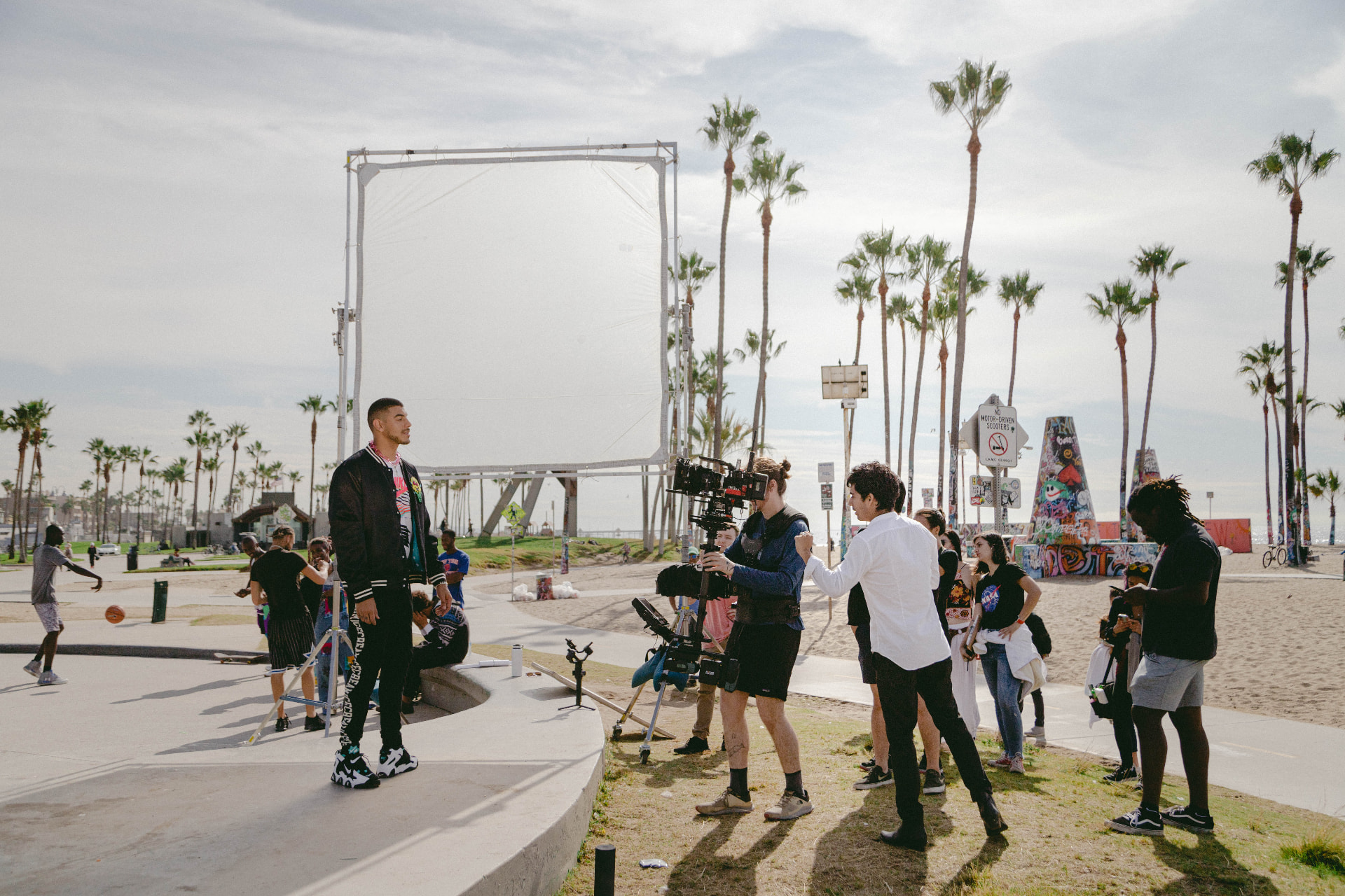Talent standing on the beachfront set as the camera team lines up a shot.